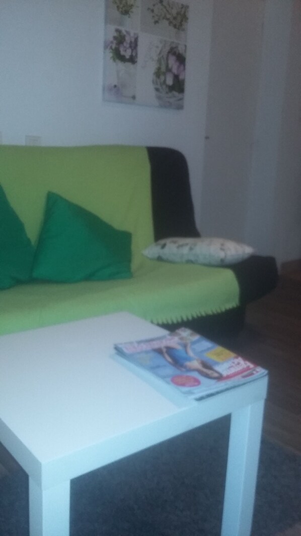 Une pièce avec un canapé vert, une table basse blanche et un magazine posé sur la table.