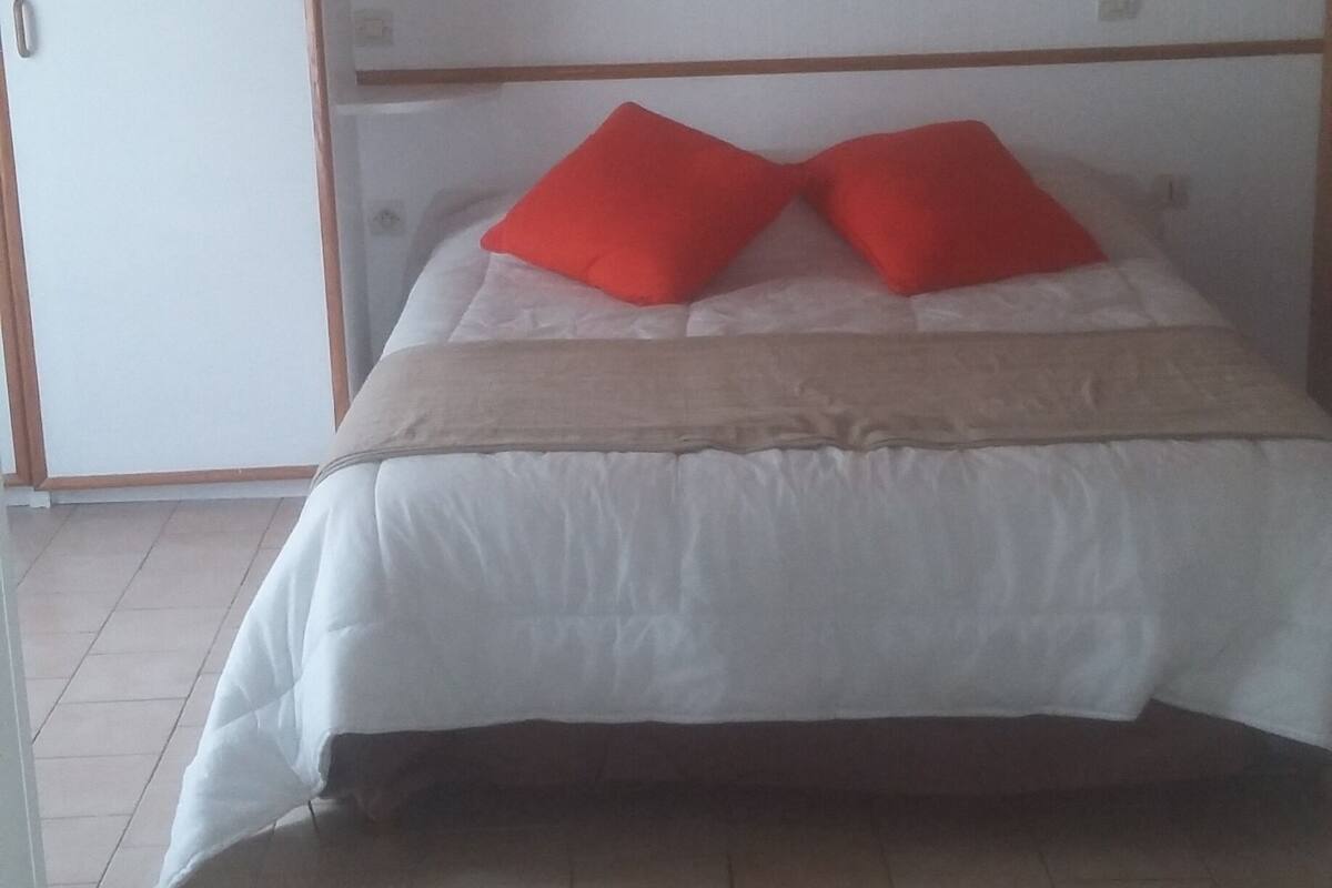 Ein Schlafzimmer mit einem Bett, zwei roten Kissen, einem hölzernen Kopfteil und einem weißen Kleiderschrank.