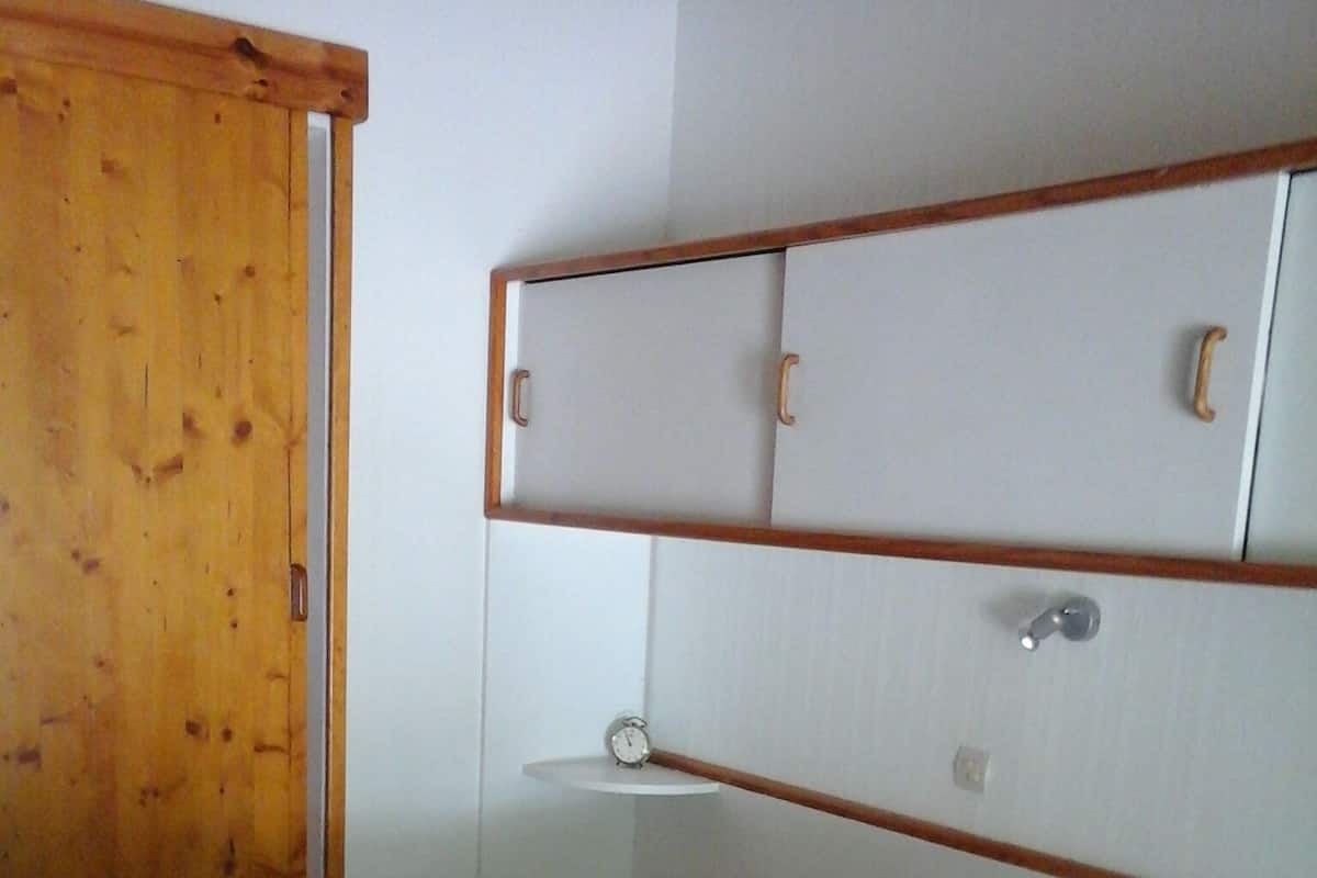 Ein Schlafzimmer mit Holztür, einem Bett mit weißer Bettwäsche und roten Kissen sowie einem weißen Nachttisch mit einer Uhr.