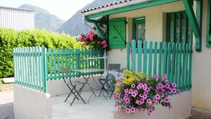 A small building with a green exterior, a patio with a table and chairs, and a flower box with pink flowers. - Le Hameau de la Courbière (Tarascon-sur-Ariege)