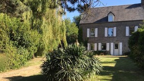 A two-story stone house with a well-maintained lawn and a large bush in the foreground. - COMFORTABLE HOUSE CLOSE TO ALL AMENITIES (Blainville-sur-Mer)
