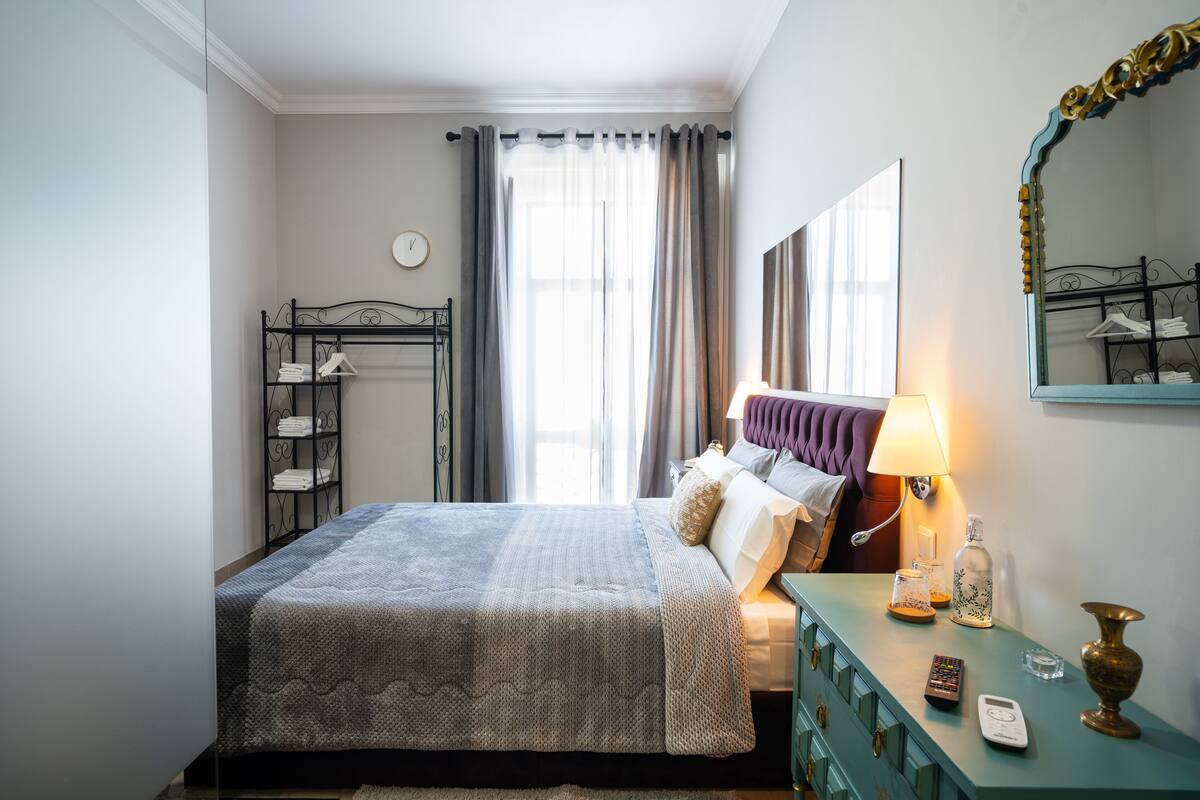 A neatly arranged bedroom with a bed, bedside table, lamp, and a mirror.