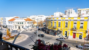 A street view with buildings, a roundabout, and a flower arrangement on a balcony. - Downtown Loulé  (Loulé)