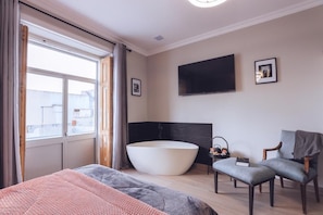 A modern hotel room with a large bed, a bathtub, a TV, and a view of the city. - Downtown Loulé  (Loulé)
