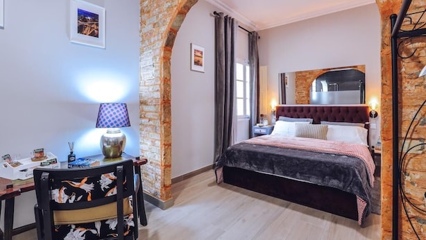 A bedroom with a brick archway, a bed with a dark headboard, a desk with a lamp, and a clock on the wall. - Downtown Loulé  (Loulé)