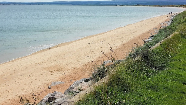 Una playa con vista despejada al agua y colinas lejanas.