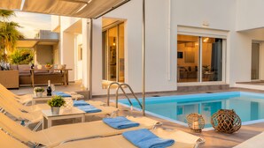 A poolside area with lounge chairs, a table with a bottle of wine, and a view of the interior of the building.
