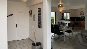 A modern kitchen with a clock, dining area with chairs and a table, and a potted plant in the hallway.