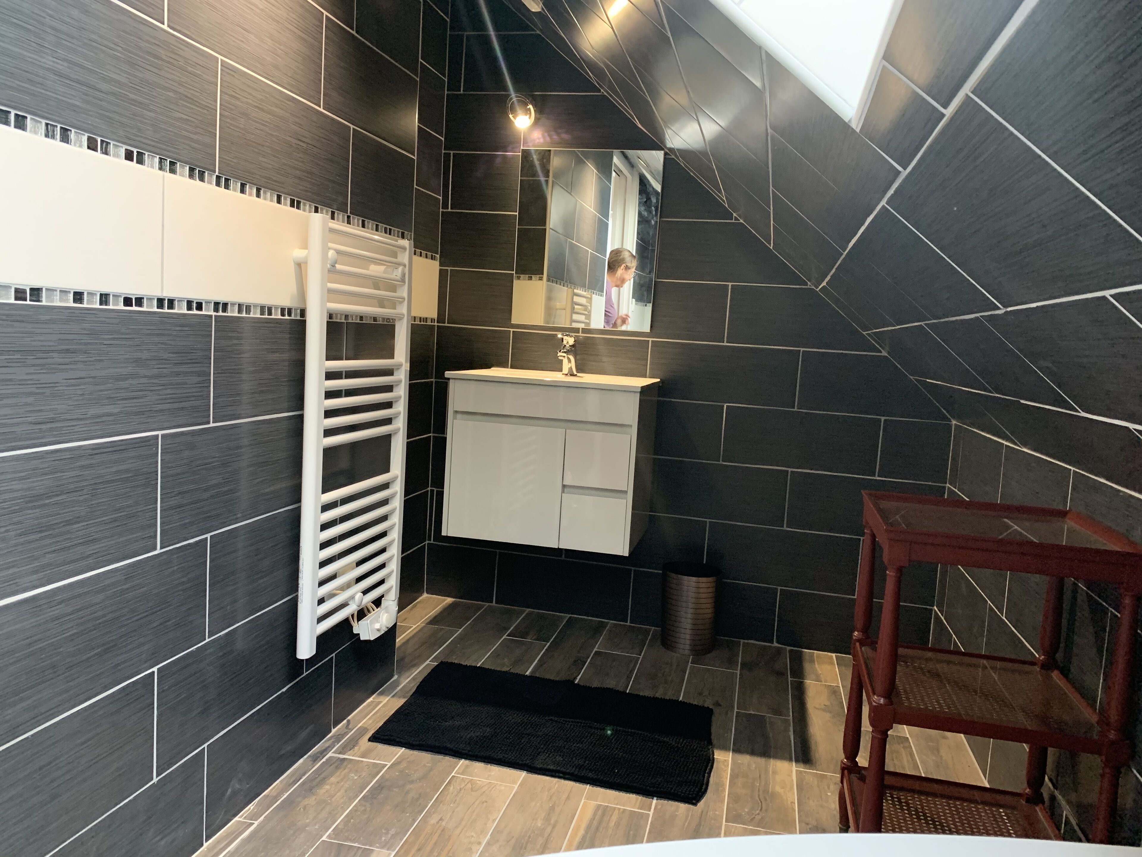 A modern bathroom with dark tiles, a white sink, and a mirror.
