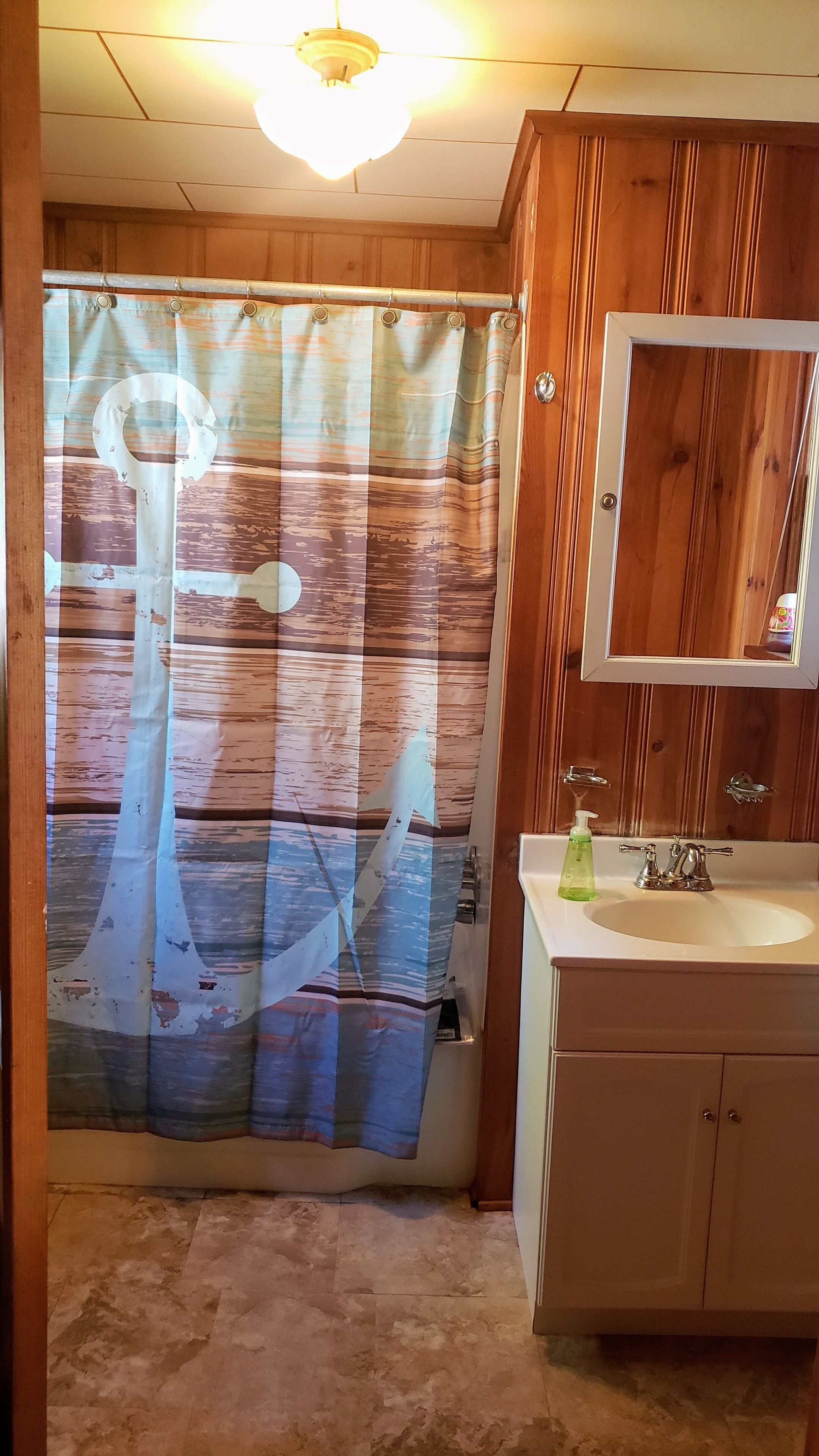 A bathroom with a wooden vanity, a sink, a mirror, and a shower curtain with a nautical design.