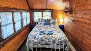 Une pièce aux murs lambrissés, comprenant un lit, deux tables de chevet, une lampe et une fenêtre avec des rideaux.