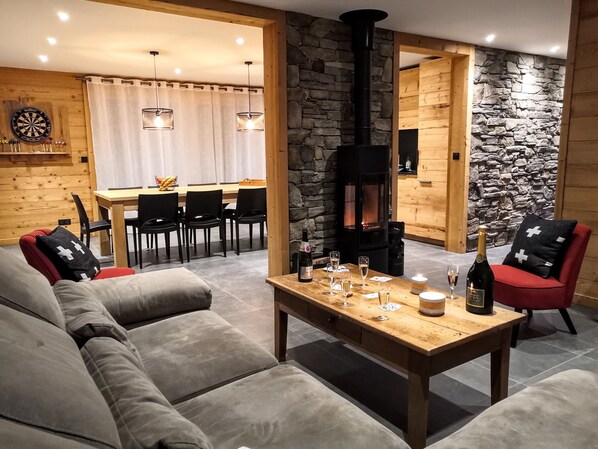 A cozy living room with a sofa, a dining area with chairs, a table with drinks, and a stone wall.