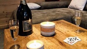 Un intérieur en bois avec une bouteille de champagne, deux verres, une bougie et un jeu de cartes sur une table.