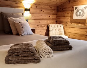 A cozy wooden cabin room with a bed, two pillows, a bedside lamp, and a wall art piece.