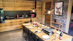 Une cuisine moderne avec des meubles en bois, un coin repas avec une table en bois dressée pour quatre personnes, et un mur en pierre orné d’un tableau.