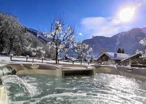 A spa area with a hot tub surrounded by snow-covered trees and mountains in the background.