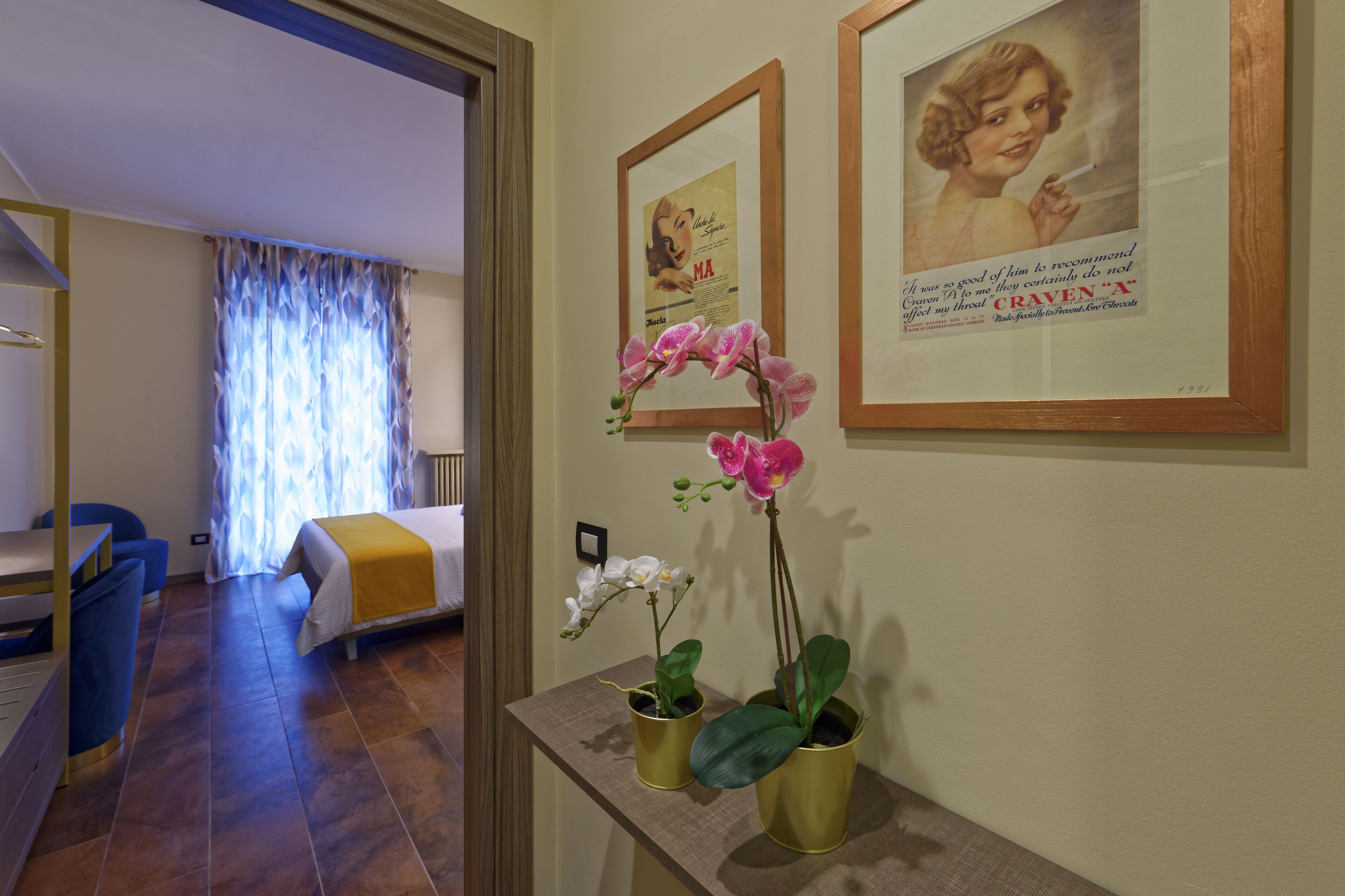 A hotel room with a bed, a desk, a chair, and two potted orchids on a small table.