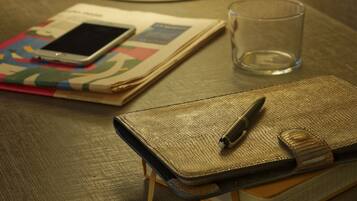 Un tavolo con una lampada, un bicchiere d'acqua, un quaderno, una penna e uno smartphone.