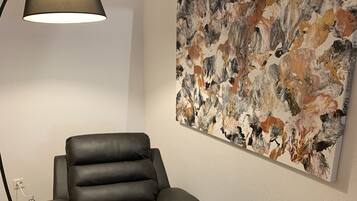Una silla de cuero negro con reposapiés, una lámpara de pie y un cuadro abstracto grande en la pared.