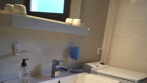 Un baño moderno con un lavamanos blanco, un espejo, un dispensador de jabón, un jabonera azul y una lavadora.