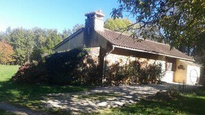 Una casa de piedra rústica con techo de tejas, rodeada de césped y árboles.