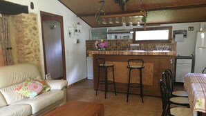 Una sala acogedora con un sofá, una mesa de centro de madera y un comedor con mesa y sillas. Se ve una cocina con una barra y taburetes al fondo.