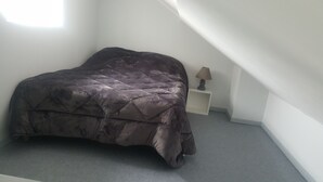 A single bed in a room with a sloped ceiling, a small bedside table with a lamp, and a plain wall. - Apartment 100 m from the beach (Les Sables-d'Olonne)