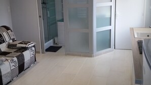 A modern kitchen with white cabinets, a built-in oven, and a countertop. There is a dining area with a sofa and a coffee table. - Apartment 100 m from the beach (Les Sables-d'Olonne)