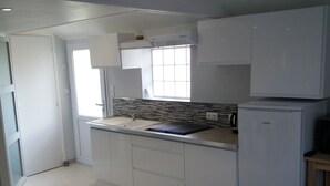 A modern kitchen with white cabinets, a built-in stove, and a refrigerator. There is a window providing natural light and a door leading to another room. - Apartment 100 m from the beach (Les Sables-d'Olonne)