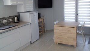 A modern kitchen with white cabinets, a built-in oven, and a coffee maker. There is a wooden table with chairs and a TV mounted on the wall. - Apartment 100 m from the beach (Les Sables-d'Olonne)