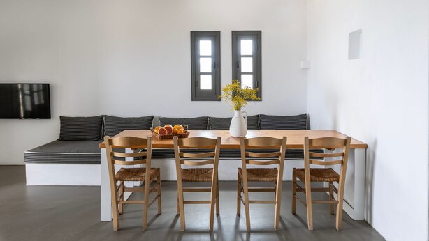 A modern kitchen with a wooden dining table, four chairs, a vase with flowers, and a built-in bench with cushions. - Indigo 4 Bedroom Villa Sea View Private Pool (Paros)