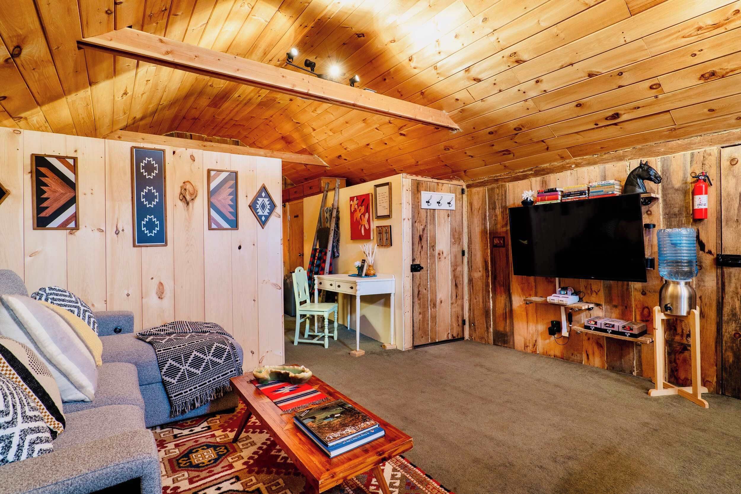 A cozy cabin interior with a sofa, a coffee table with books, a flat-screen TV, and a mounted water dispenser.