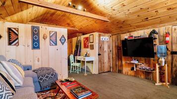 A cozy cabin interior with a sofa, a coffee table with books, a flat-screen TV, and a mounted water dispenser.