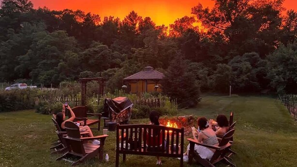 A group of people seated around a fire pit in a garden with a gazebo and trees in the background. - Farm - Animals - Barn - Gazebo - Fire Pit - 2xKing (Willington)