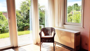 Ein Zimmer mit einer großen Schiebeglasdoor, einem Korbstuhl, einer Heizung und einem Fliesenboden.