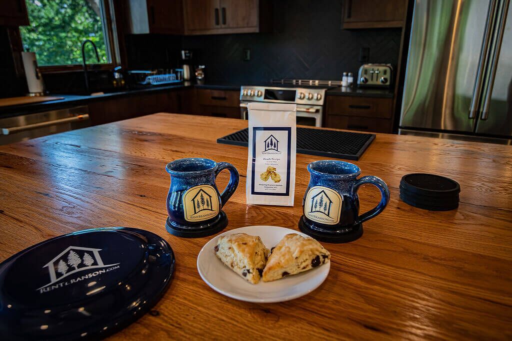Un comptoir de cuisine en bois, avec deux tasses bleues, une assiette contenant deux pâtisseries et un sous-verre noir orné d’un logo.