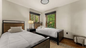Camera da letto con due letti, un comodino, una lampada e vista sul verde dalle finestre.