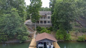A lakeside house with a dock, stone walls, and a large tree. - Tradewind Terrace-Mtn View, Kayaks, Paddleboards, Outdoor Kitchen, Generator etc (Huddleston)
