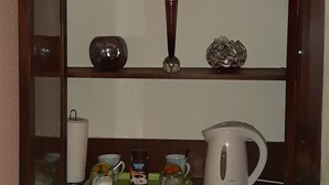 A kitchen with a wooden cabinet containing various kitchenware and a white countertop with a kettle and a floral arrangement. - Phoenix Guest House (Barrow-in-Furness)