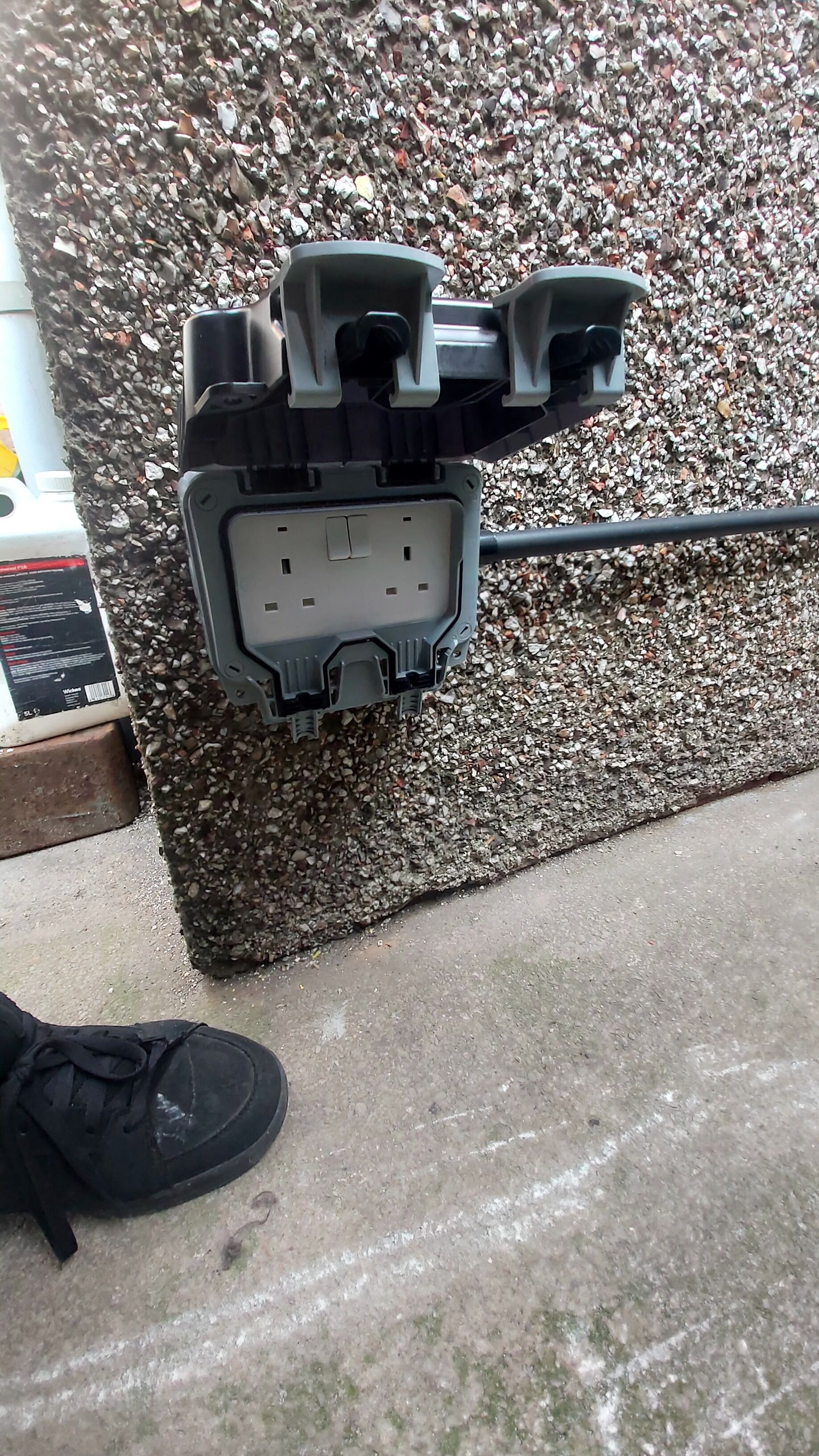 A black electrical outlet box mounted on a wall with a rough, pebble-textured surface.