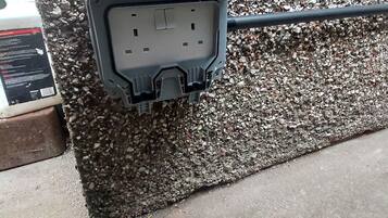 A black electrical outlet box mounted on a wall with a rough, pebble-textured surface.
