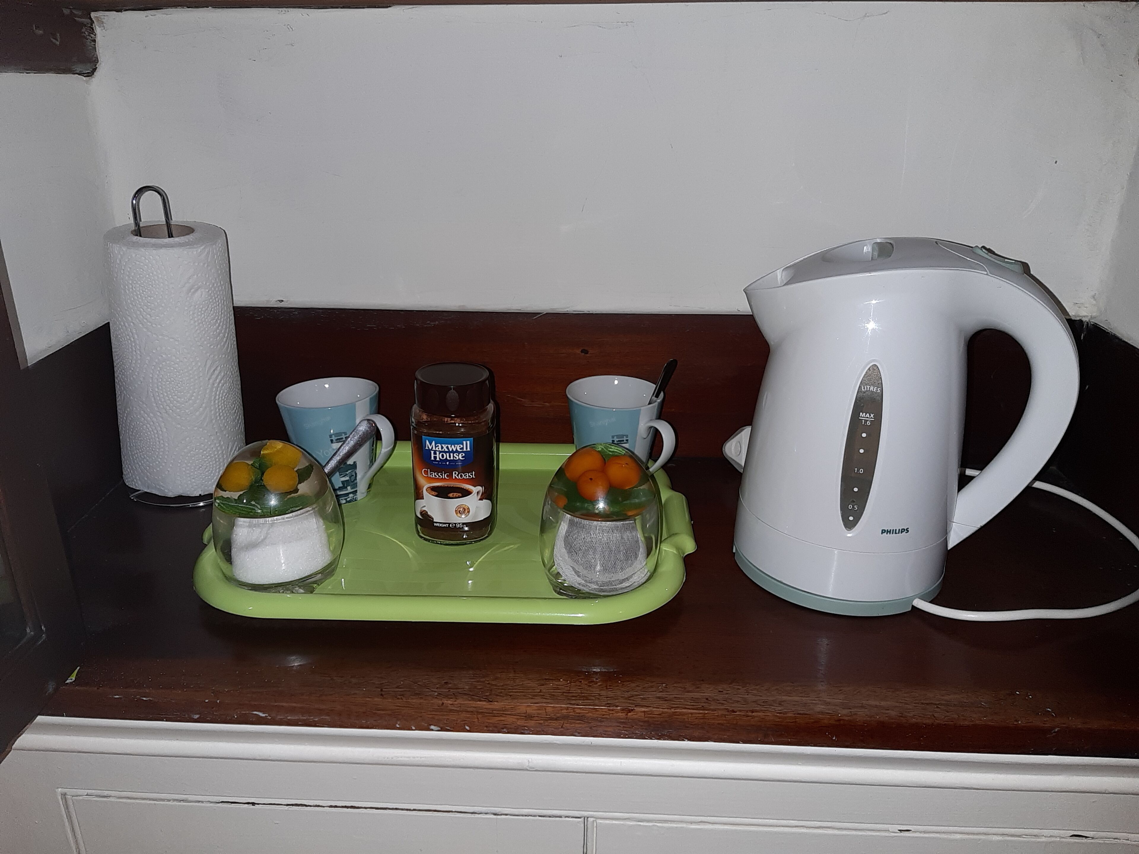 Un comptoir de cuisine avec une bouilloire blanche, un plateau vert sur lequel se trouve une machine à café, un bocal de café et deux tasses.