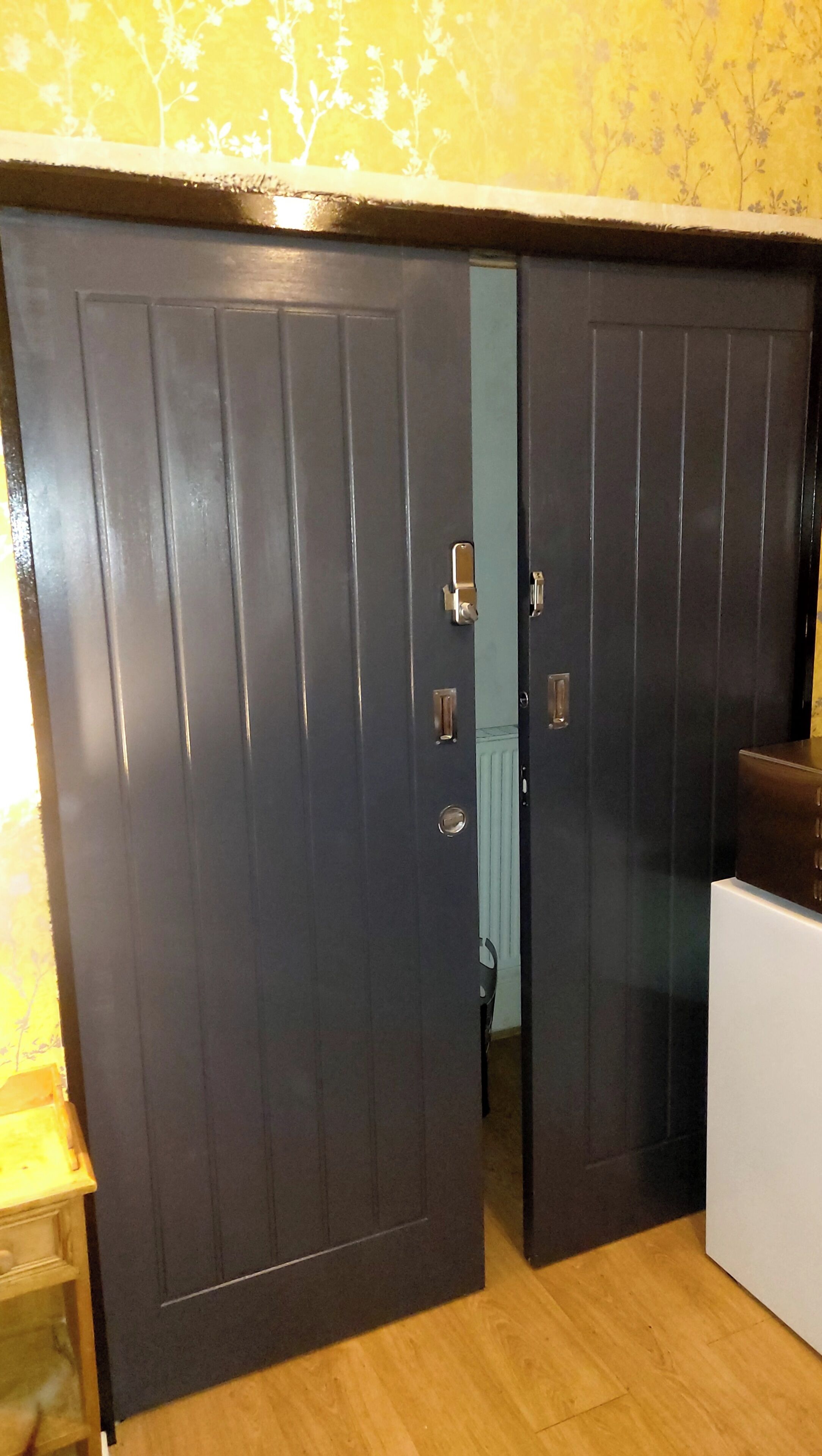 Um quarto com piso de madeira, um guarda-roupa escuro e um armário branco.