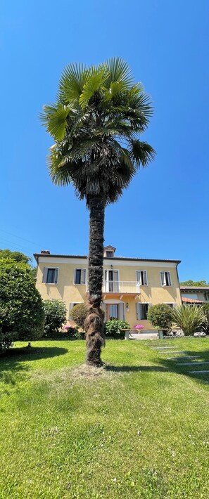 Ein zweistöckiges Gebäude mit Balkon, umgeben von einem gepflegten Rasen und einer Palme.