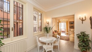 A dining area with a round table and white chairs, a potted plant, and a view of the adjacent living room. - Ripetta Deluxe Terrace (Rome)