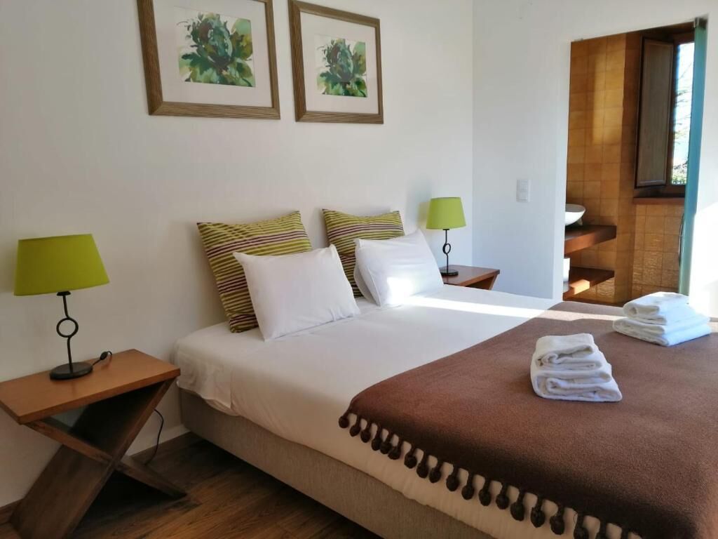 Habitación de hotel con una cama, dos mesitas de noche con lámparas, una manta marrón y vistas a una escalera de madera.