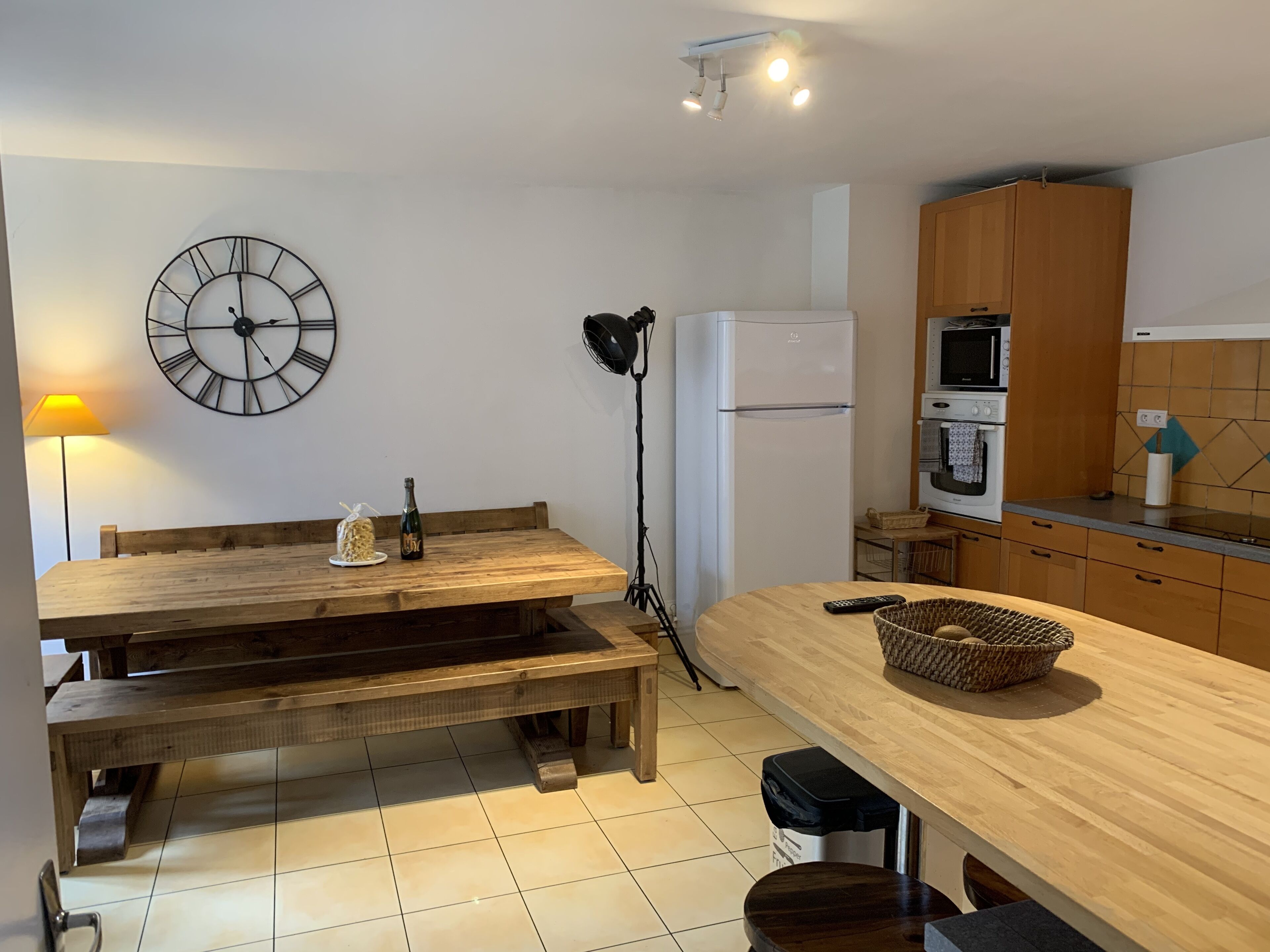 Une cuisine de taille réduite avec une table en bois, une horloge et un réfrigérateur.