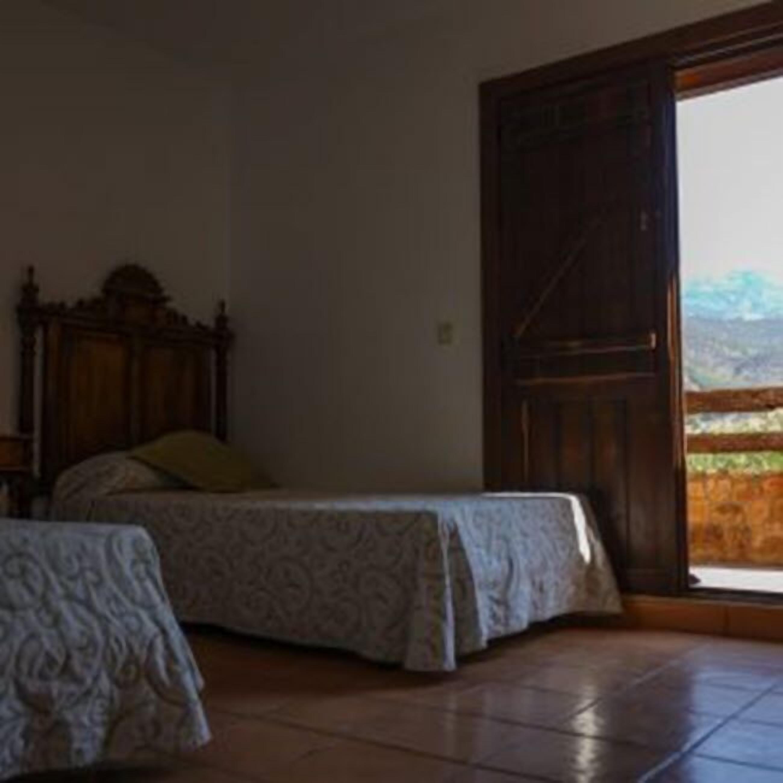 Una habitación con una cama, una mesita y una puerta grande de madera que da a un balcón.