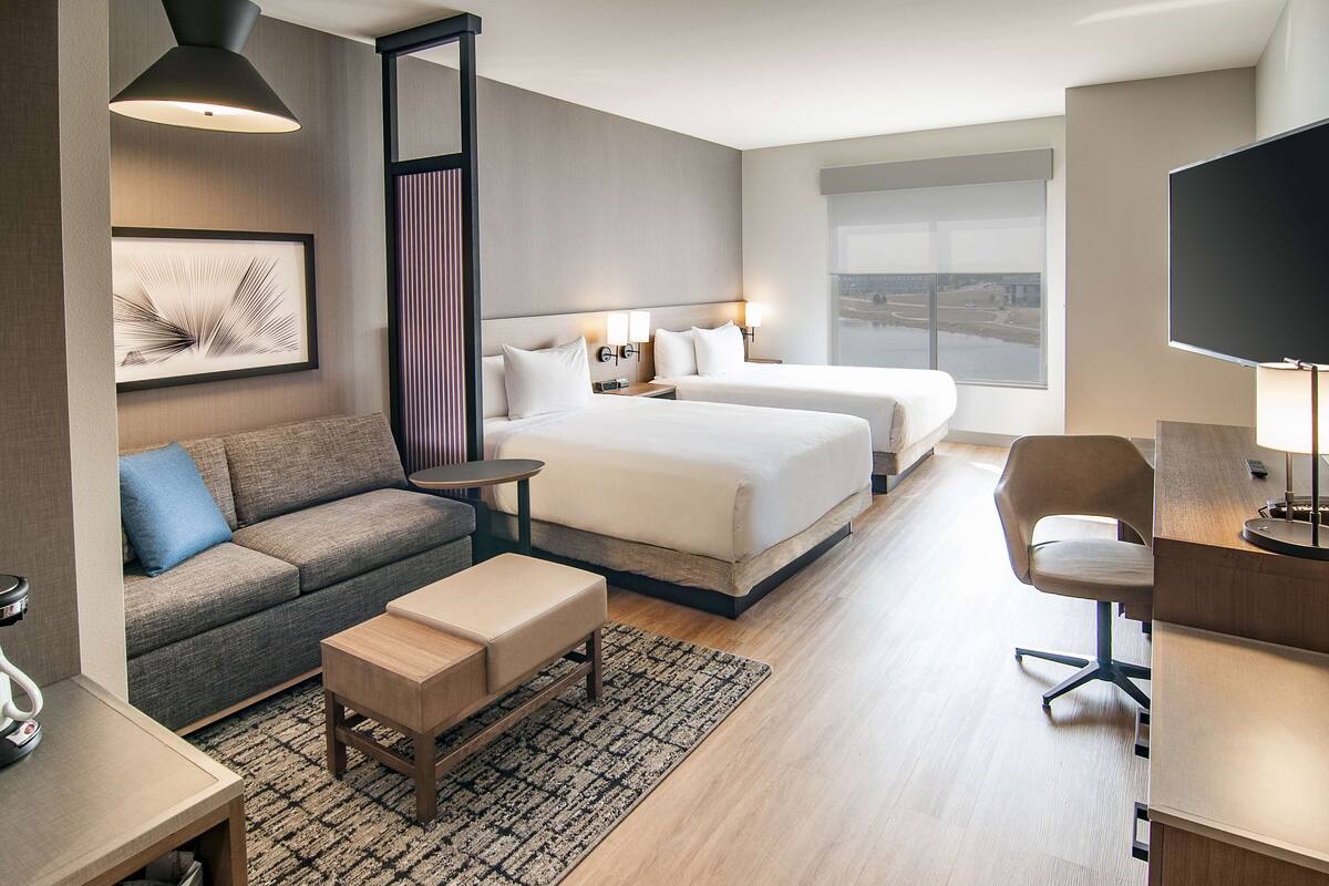 Une chambre d’hôtel moderne équipée de deux lits, d’un canapé, d’un bureau et d’une télévision.