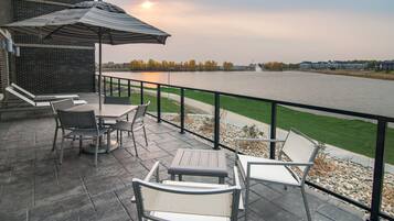 A patio with outdoor furniture, a view of a river, and a building in the background.